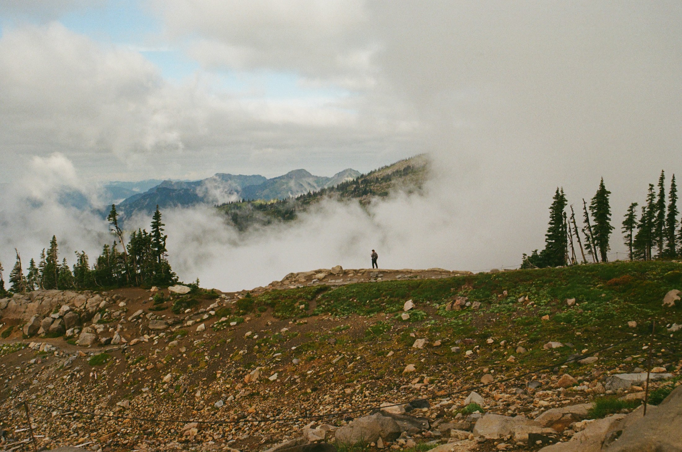 A solitary person standing in a mountain landscape as weather moves across the ridge