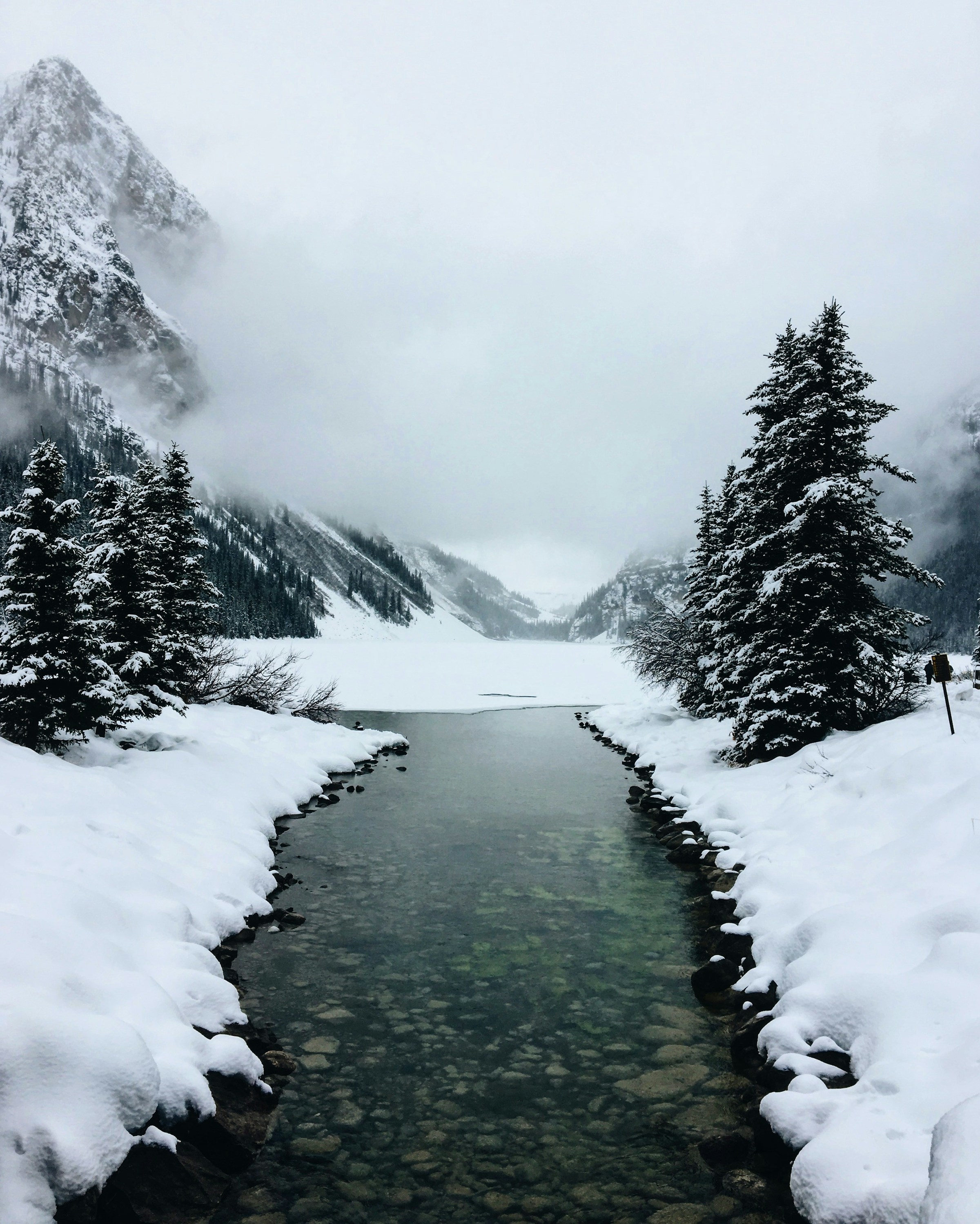 A cold mountain river running through snow and low cloud
