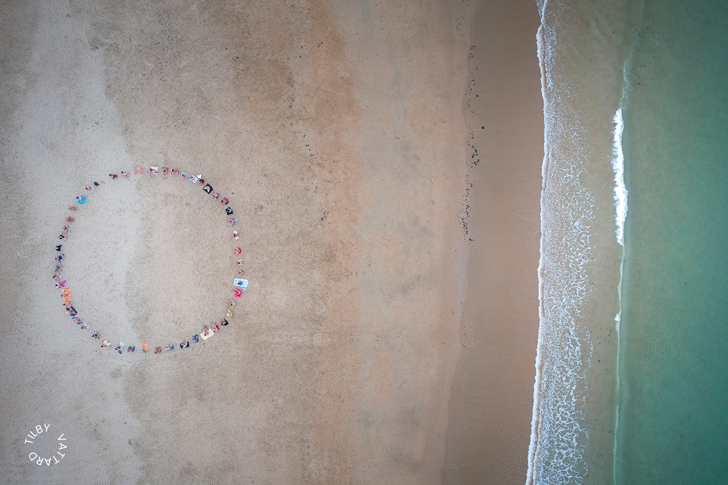 People forming a large circle on a beach beside the ocean