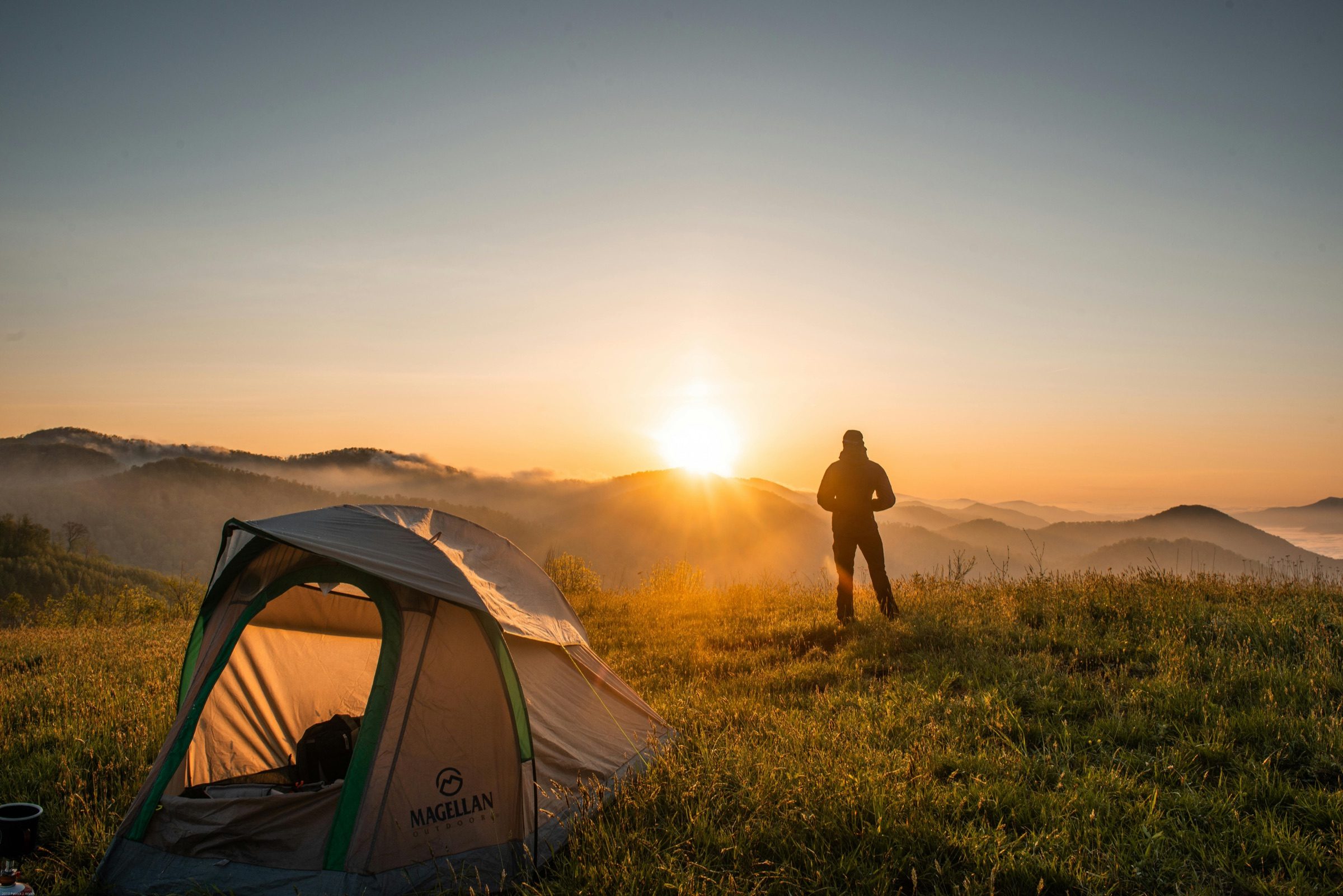 A man standing quietly beside a tent at sunrise