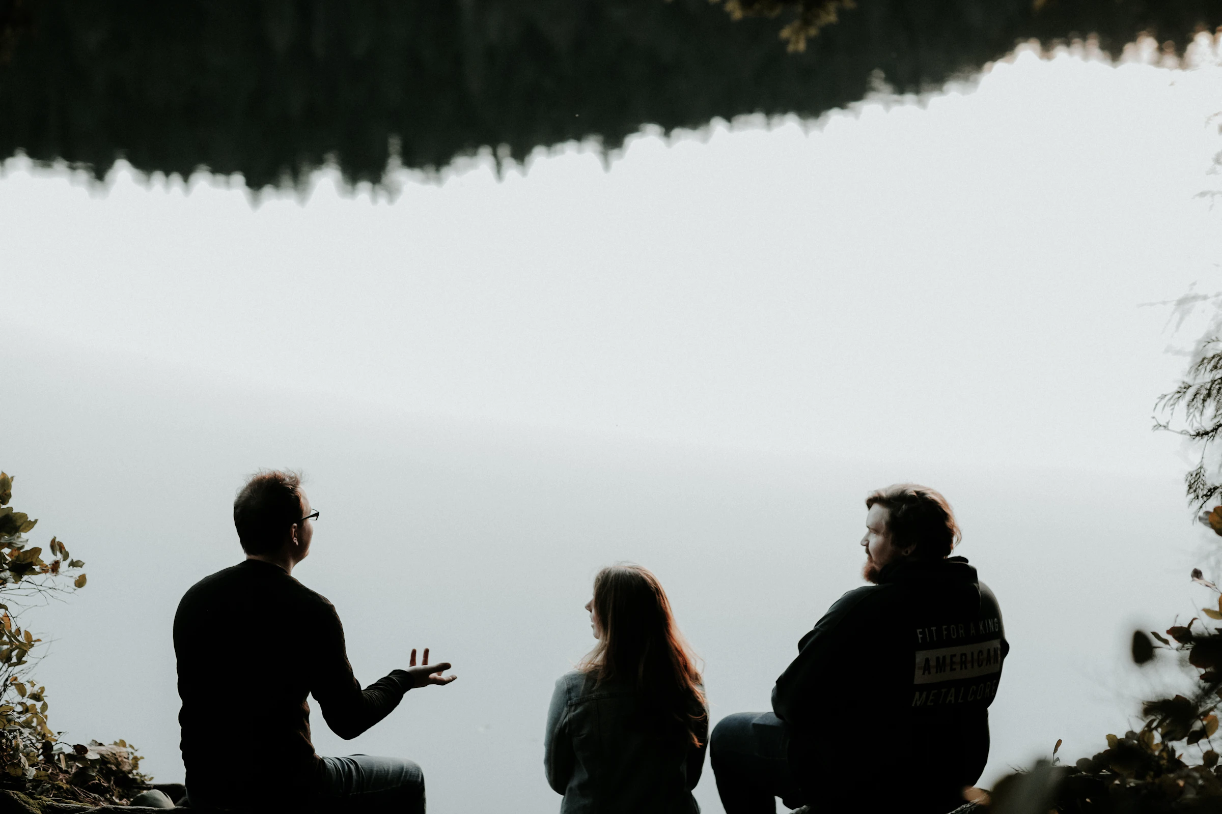 Three leaders seated together beside a quiet mountain lake