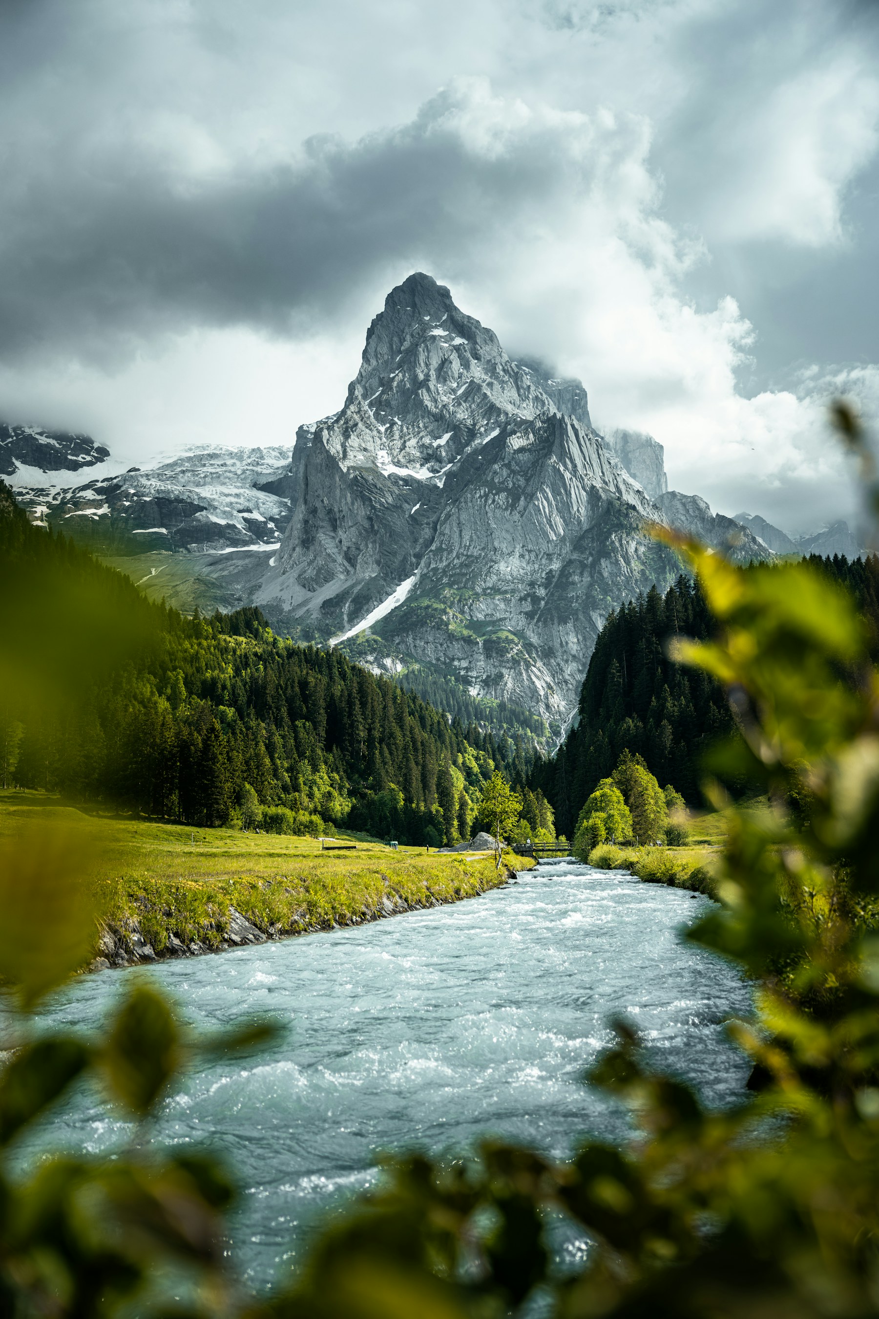 A clear mountain river moving through forest beneath a raw Alpine peak